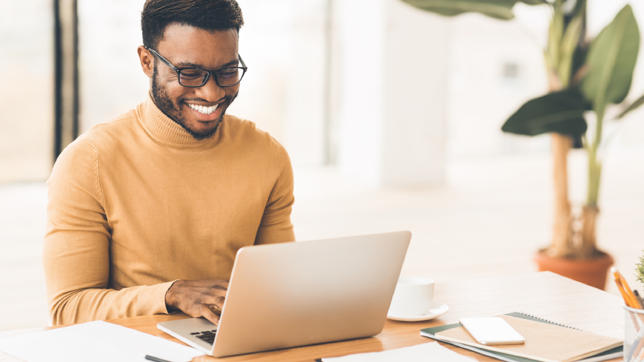 A young man sitting behind a computer with glasses on